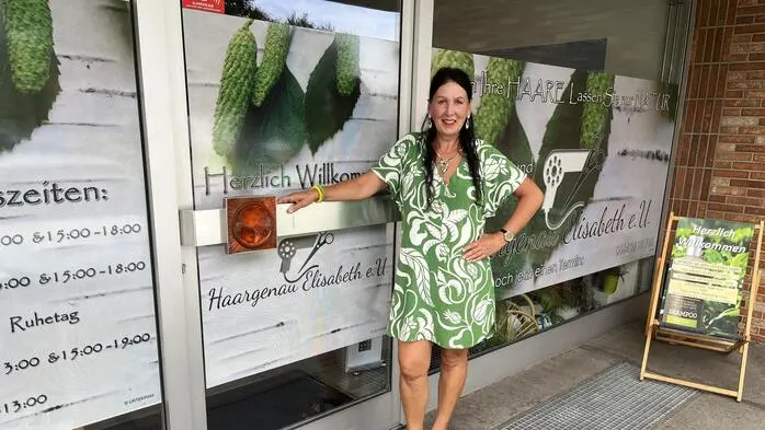 Eine Frau posiert vor dem Eingang ihres Friseursalons für ein Foto und lächelt in die Kamera.
