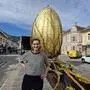 Auf dem Foto sieht man eine Frau in einem gestreiften Shirt, die auf einem Platz vor einem großen  goldenen Osterei steht und in die Kamera lächelt | Andrina Theißl und ihr Team von der Erlebnisgärtnerei Steffan gestalteten das diesjährige Osterei