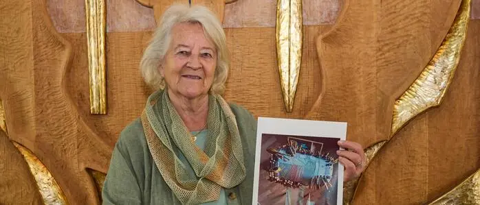 Eine Frau mit grauen Haaren hält ein Bild in der Hand und lacht in die Kamera