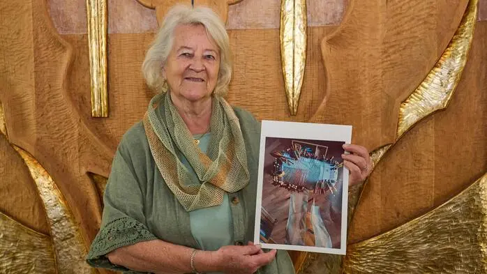 Eine Frau mit grauen Haaren hält ein Bild in der Hand und lacht in die Kamera