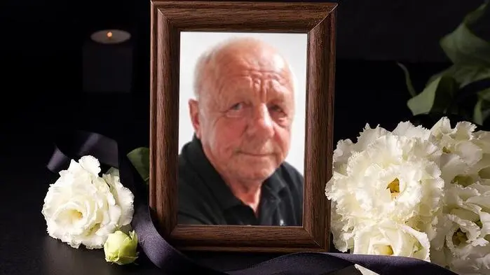 Ein Bild von einem Mann in einem Bilderrahmen, daneben liegen weiße Blumen