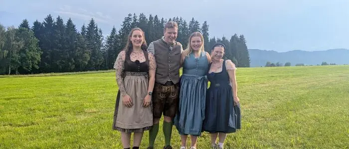 Ein Mann und drei Frauen in Tracht stehen dicht beieinander auf einer Wiese