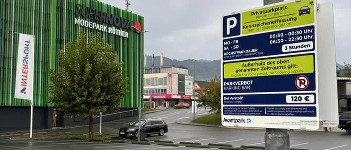 Eine Infotafel über die Parkregeln vor einem Einkaufszentrum. Im Hintergrund sieht man das Center, das in grün gehalten ist