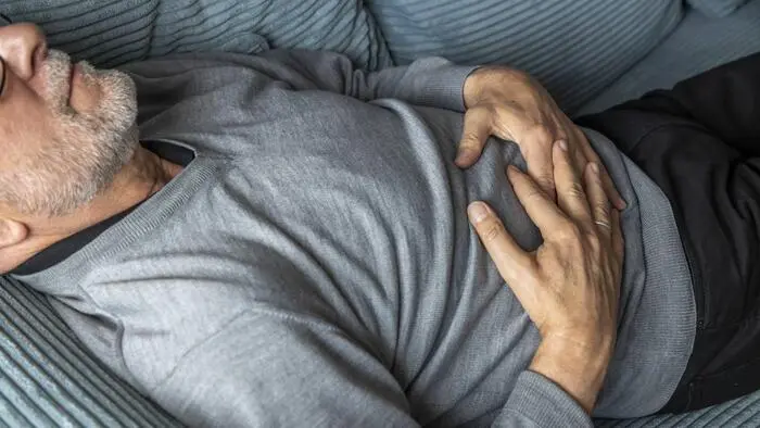 Älterer Mann liegt auf einer Couch und hält sich den Bauch.