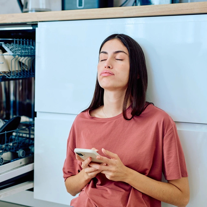 Erschöpfte Frau in der Küche mit Handy in der Hand