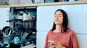 Erschöpfte Frau in der Küche mit Handy in der Hand