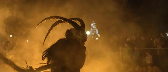 Krampus bei einem Krampuslauf mit einem bengalischen Feuer. Im Hintergrund sieht man die Zuseher hinter einem Absperrgitter. | Bengalische Feuer sind beliebte Utensilien der Krampusse (Symbolbild)