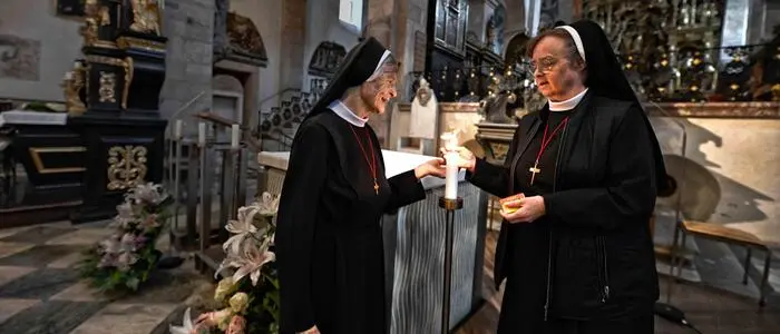 Zwei Klosterschwestern zünden eine Kerze an