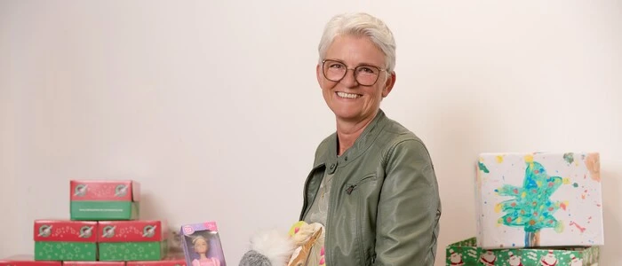 Eine Frau mit kurzen Haaren lächelt in die Kamera und hält Geschenke in der Hand.