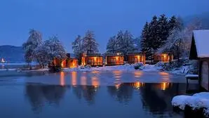 Eine winterliche Aufnahme eines Sees mit ein paar verschneiten Hütten | Das Seehotel Hoffmann ist das zweitbeliebteste Hotel in Kärnten