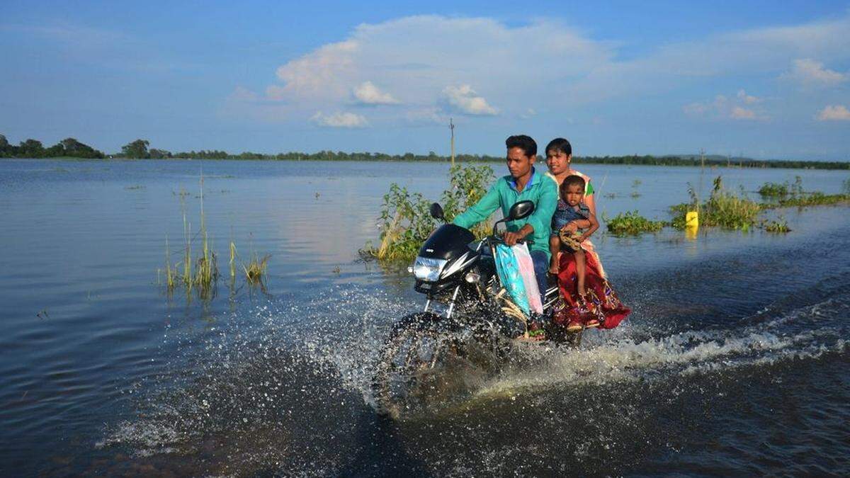 Eine indische Familie fährt entlang einer überschwemmten Straße in Assam.