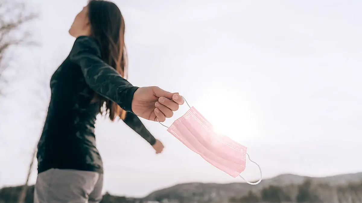 Mask PPE for coronavirus protection woman carefree happy letting go of face mask after receiving vaccine. End of pandemic.