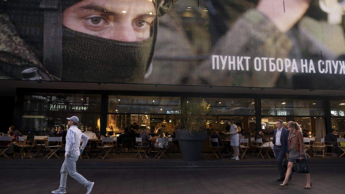 Ein Plakat vor einem Restaurant wirbt für den Kampfeinsatz. Menschen spazieren davor daran vorbei. | Ein Plakat vor einem Restaurant wirbt für den Kampfeinsatz