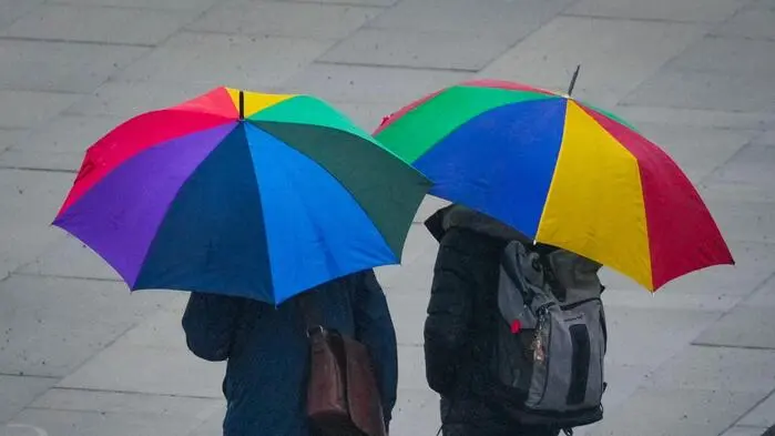 Zwei Personen mit bunten Schirmen gehen über einen gepflasterten Platz