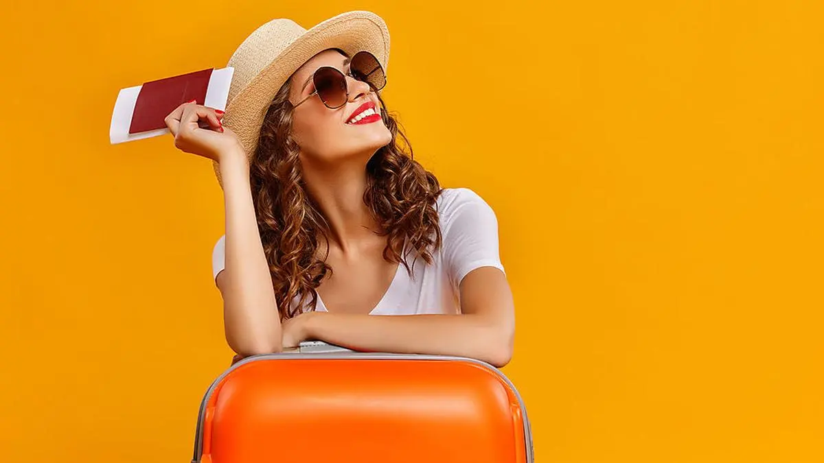 concept of travel. happy woman girl with suitcase and passport on  yellow colored background
