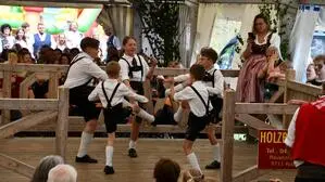 Fünf Jugendliche tanzen in traditioneller Kleidung einen Schuhplattler auf einem Tanzboden in einem Zelt