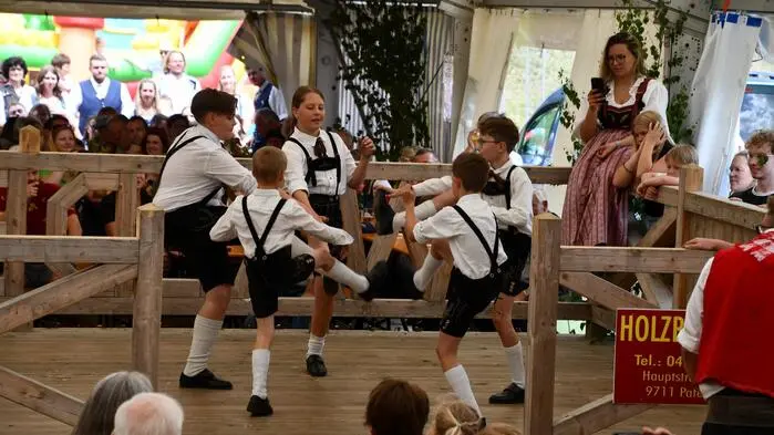 Fünf Jugendliche tanzen in traditioneller Kleidung einen Schuhplattler auf einem Tanzboden in einem Zelt