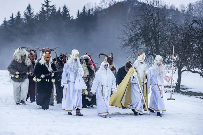 Der Apostel Thomas, der weiße Thomas, auch Lichtbringer genannt, die Nikolofrau, der Gabenbringer, auch Sackträger genannt, der Greis, die Thomashutzn sowie Krampusse unterwegs auf einer schneebedeckten Wiese