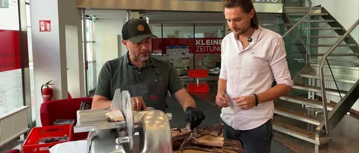Zwei Männer stehen an einem Tisch. Auf dem Tisch liegen verschiedene Speckwaren.
