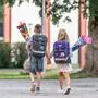 Zwei Kinder gehen Hand in Hand mit ihren Schultüten eine Straße entlang