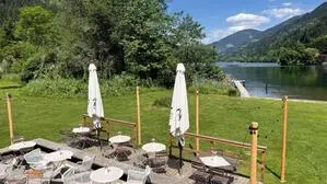 Ein Gastgarten auf einer Wiese, im Hintergrund ein See und Berglandschaft