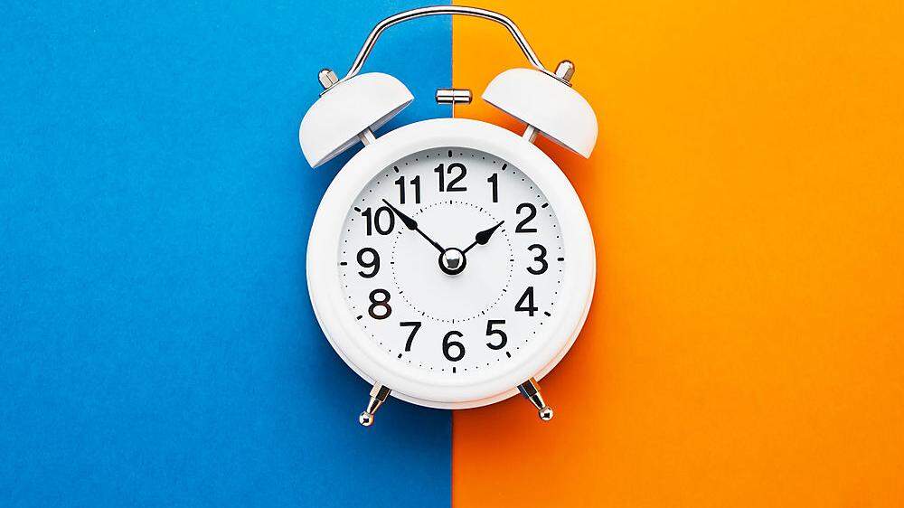 White vintage alarm clock on blue-orange background. Top view, copy space. Daylight saving concept.
