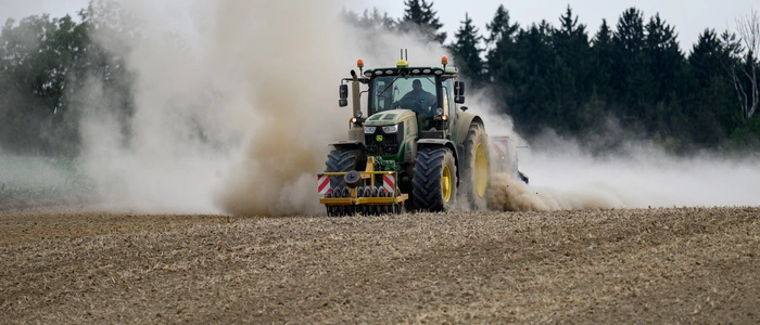 Ein Traktor mit landwirtschaftlichen Anbaugeräten und Sämaschine bearbeitet einen trockenen Acker. Durch die Feldarbeit entstehen große Staubwolken. Die Aufnahmen zeigen moderne Landwirtschaft und Bodenbearbeitung unter trockenen Bedingungen.