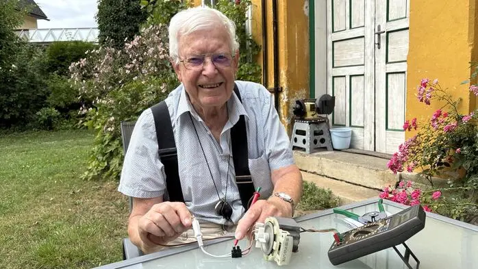 Ein älterer Mann mit Brille sitzt an einem Tisch und bedient ein elektrisches Gerät