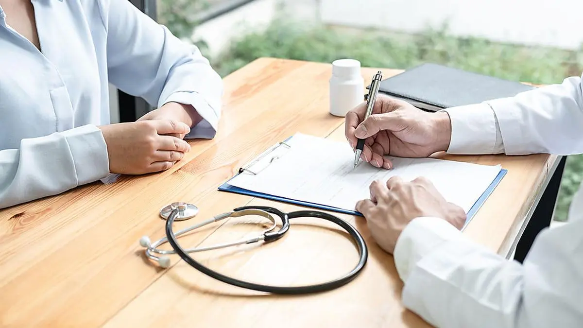 Male doctor with stethoscope is writing symptom of patient medication history and prescription on clipboard while explaining treatment and giving recommendation to patient in clinic