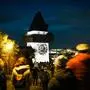 Der Grazer Uhrturm, fotografiert nachts, beleuchtet mit einer Lichtinstallation, rundherum viele Menschen