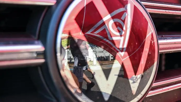 Eine Fahne der IG Metall spiegelt sich in einem VW-Logo | Sommerliche Großkampftage der Gewerkschaft: gleich neun Betriebsversammlungen bei Volkswagen stehen an