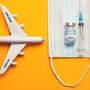 Travel during covid-19 pandemic. Airplane model, protection medical mask, vaccine and syringe on yellow background.