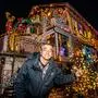 Ein Mann vor einem weihnachtlich bunt-leuchtend dekorierten Haus im Winter