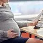 pregnancy, business and work concept - smiling pregnant businesswoman sitting at office table and reading papers
