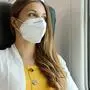 Travel safely on public transport. Young woman with KN95 FFP2 face mask looking through train window. Train passenger with protective mask travels sitting in business class looking through the window.