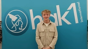 Ein junger Schüler steht vor einem Banner, auf dem HAK 1 steht