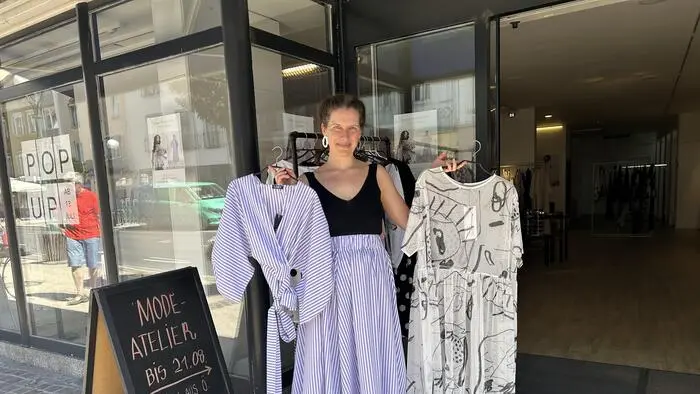 Eine Frau hält vor einem Geschäft Kleidungsstücke in der Hand