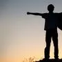 Boy playing superheroes on the sky background, silhouette of teen superhero in a raincoat on the hill