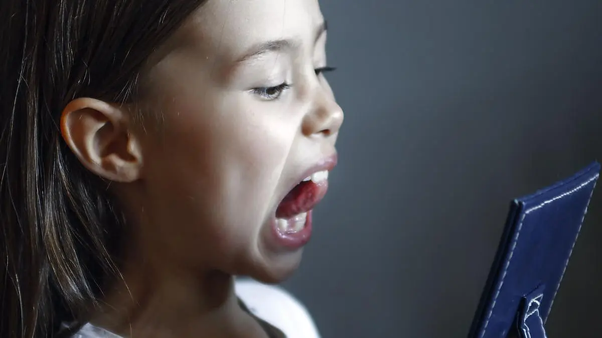 The girl in front of the mirror does logopedic exercises. Gymnastics for the tongue