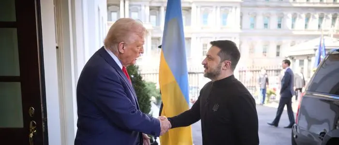 Donald Trump und Wolodymyr Selenskyj schütteln sich die Hände. Im Hintergrund hängt eine ukrainische Flagge.