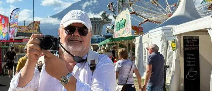 Ein Mann mit weißem Hemd, Brille und Kappe hält eine Kamera hoch, im Hintergrund das Marktgelände