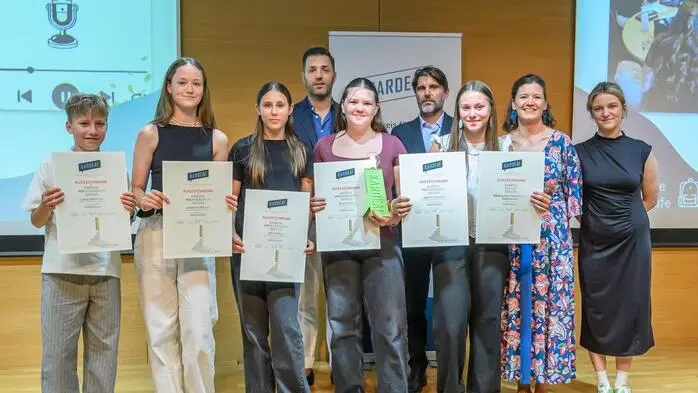 Einige Schülerinnen und Schüler lächeln in die Kamera und halten eine Auszeichnung in ihren Händen.