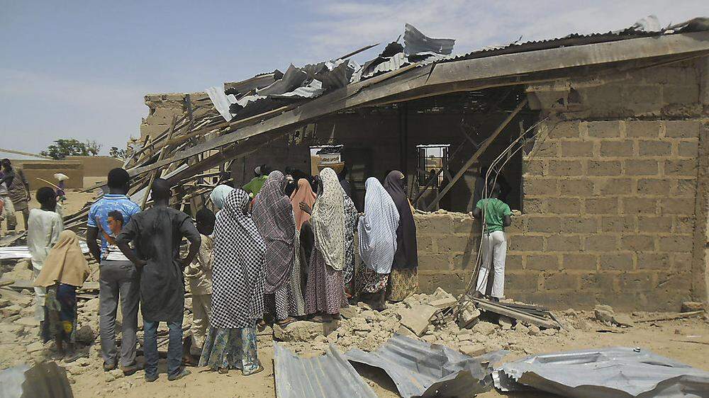 Nigerianer stehen vor den resten eines Hauses, das bei einem Anschlag am Wochenende zerstört wurde
