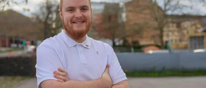 Ein lächelnder Mann mit rotem Bart und weißem Hemd vor einem Wohngebiet