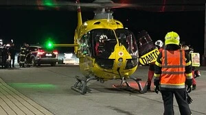 Ein gelber Rettungshubschrauber steht auf einem Betonplatz, davor ist ein Feuerwehrmann in oranger Weste und gelbem Helm von hinten zu sehen