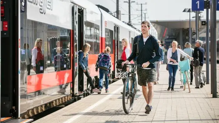 Ein Mann mit einem Fahrrad steht an einem Bahnsteig, an dem gerade ein Zug hält