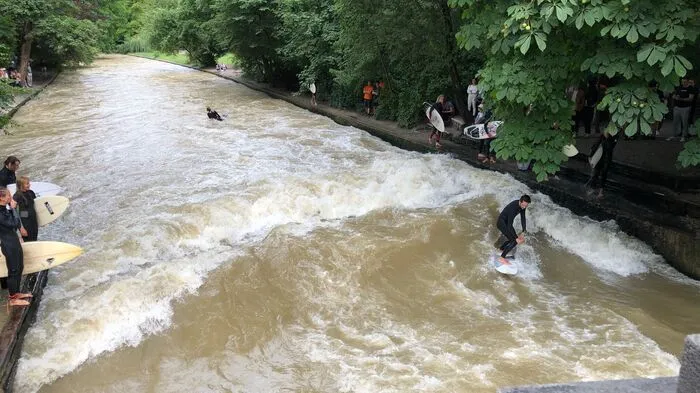 An der Eisbachwelle in München gelten klare Regeln: abwechselnd von links und rechts geht jemand ins Wasser