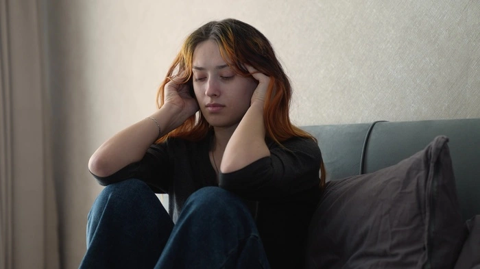 Eine junge Frau sitzt auf einem Sofa. | Kinder und Jugendliche benötigen vermehrt Unterstützung wegen psychischer Problemstellungen