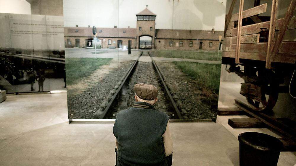 Ein ehemaliges Holocaust-Opfer vor einem Foto des KZ Auschwitz 