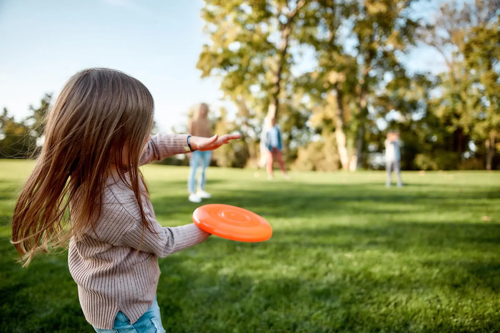 Portrait of happy family of four playing with disc on a green meadow with grass. Focus on daughter. Family, kids and nature concept. Horizontal shot. Rear view